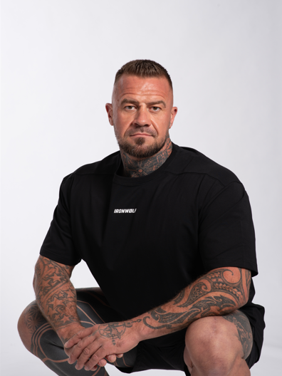 Man in black gym wear with tattoos, crouching confidently in activewear for training and lifestyle