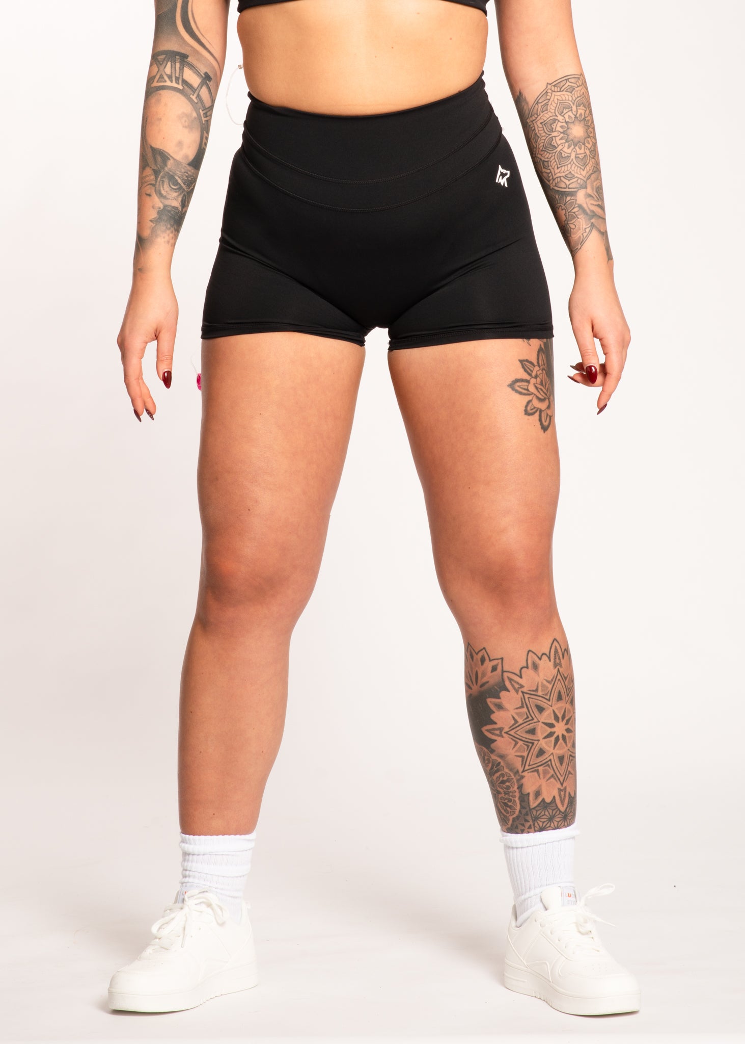 Black high-waisted gym shorts with logo, worn with white sneakers and socks, ideal for training and active lifestyle.