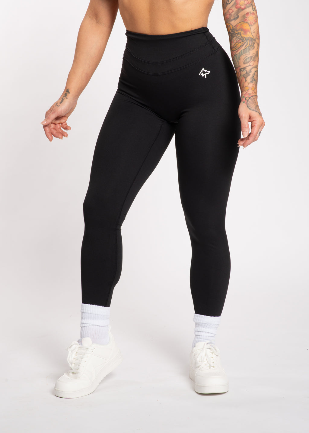 Black high-waisted gym leggings with white logo, paired with white sneakers and socks, ideal for training and active lifestyle.