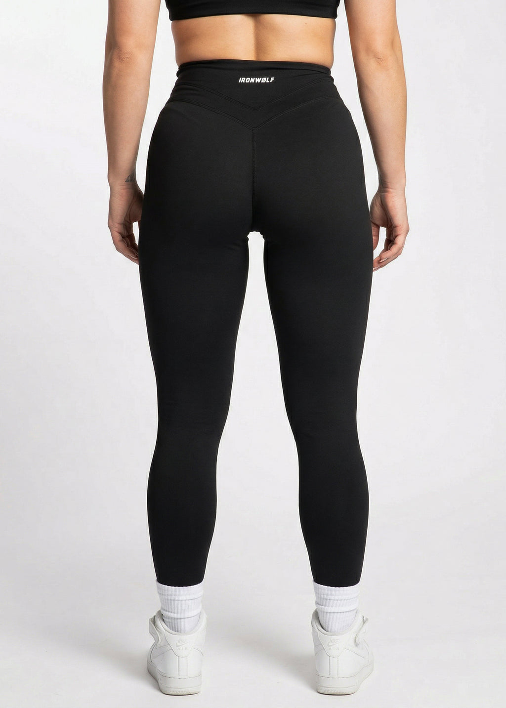 Black high-waisted gym leggings with IRONWØLF waistband, paired with white sneakers for training or lifestyle wear.
