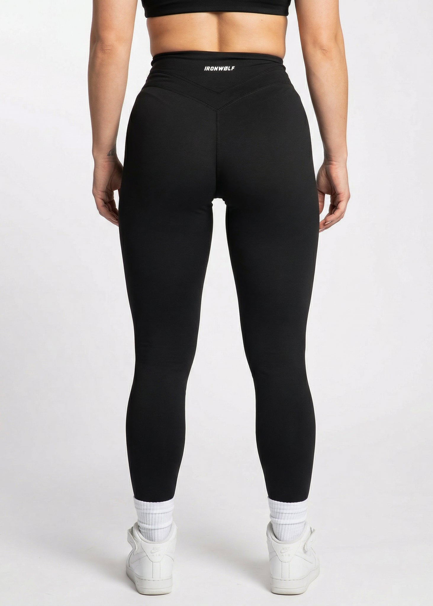 Black high-waisted gym leggings with IRONWØLF waistband, paired with white sneakers for training or lifestyle wear.