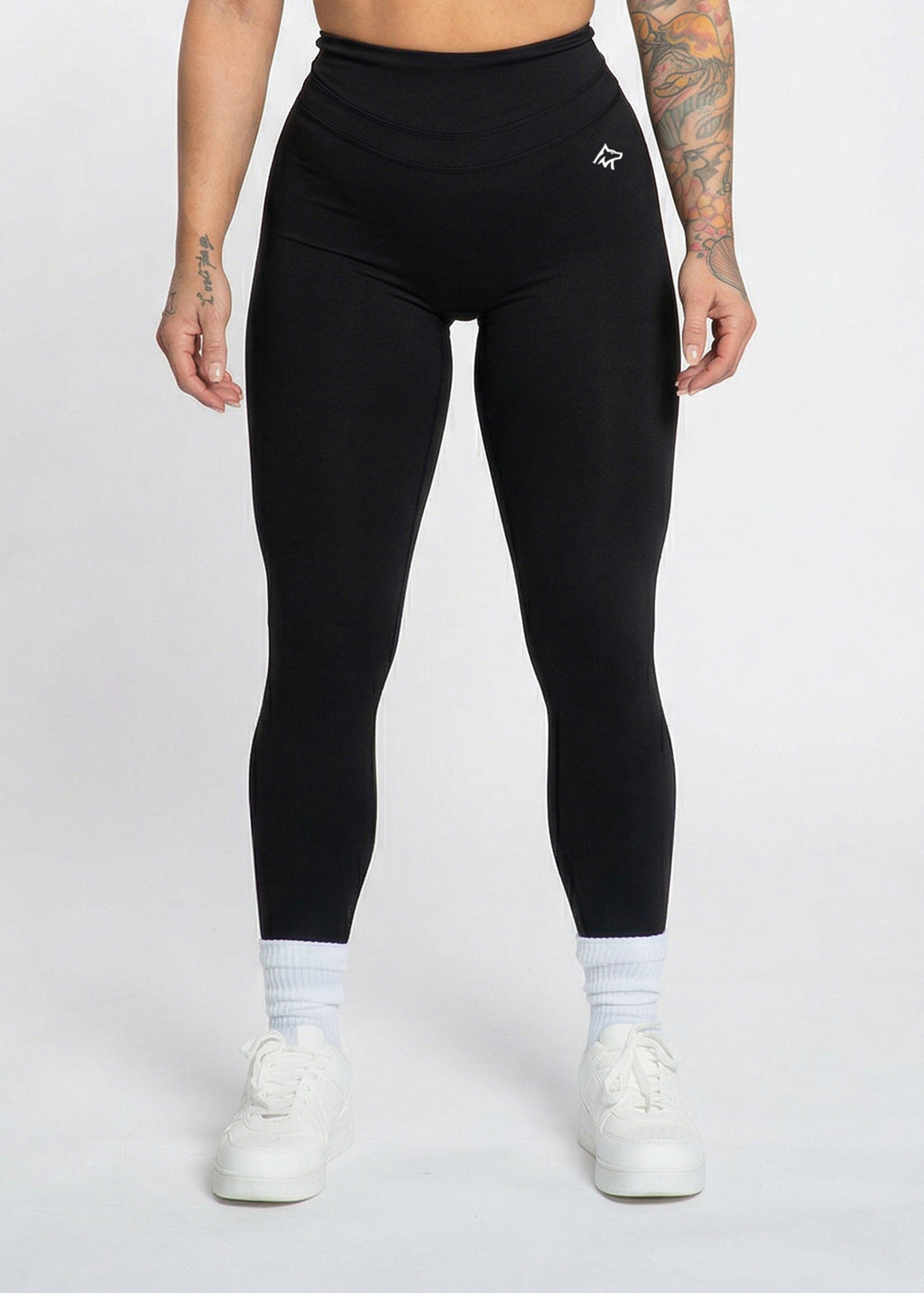 Black high-waisted gym leggings with white logo, worn with white sneakers and socks for workout or casual wear