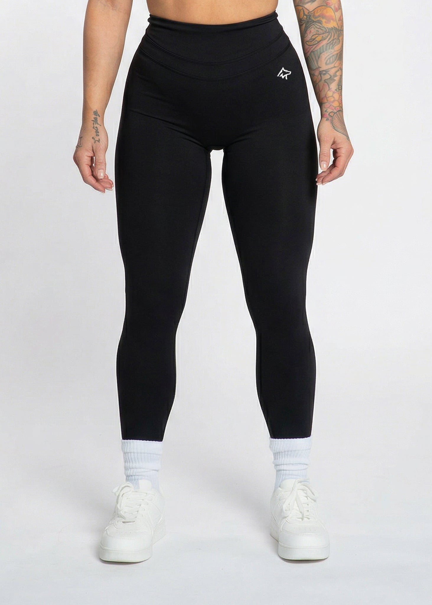 Black high-waisted gym leggings with white logo, worn with white sneakers and socks for workout or casual wear