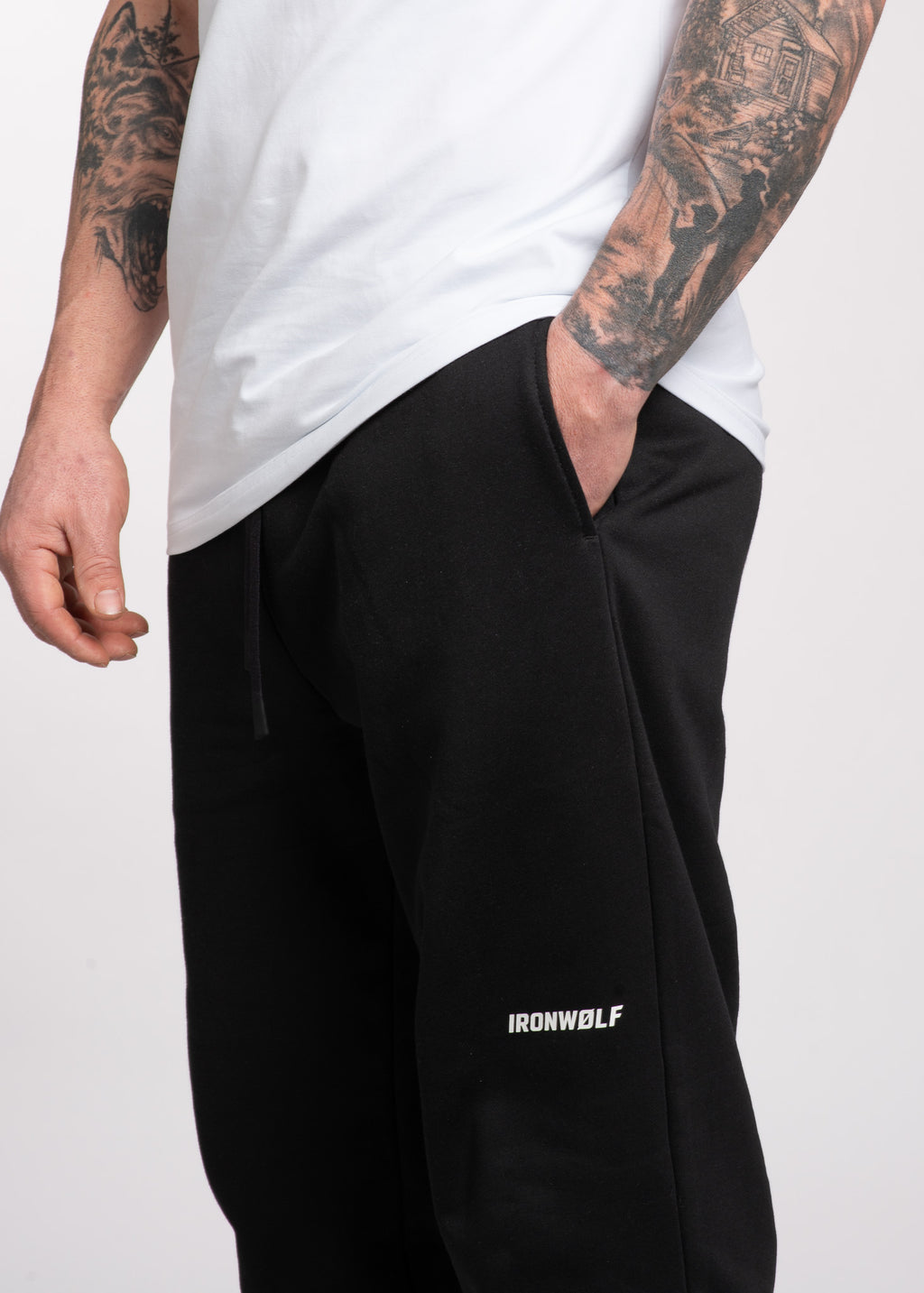 Man wearing black IRONWØLF sweatpants with white logo, paired with white tee, showcasing gym wear for training and lifestyle.