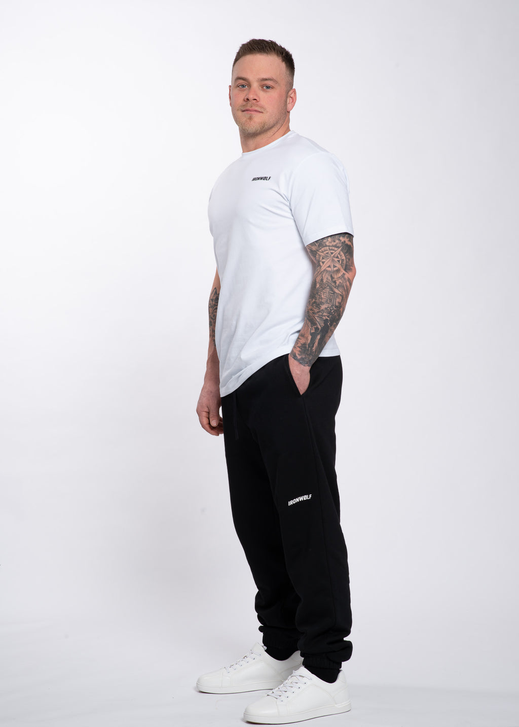 Man in white IRONWØLF tee and black joggers, showcasing gym wear for training and lifestyle comfort.