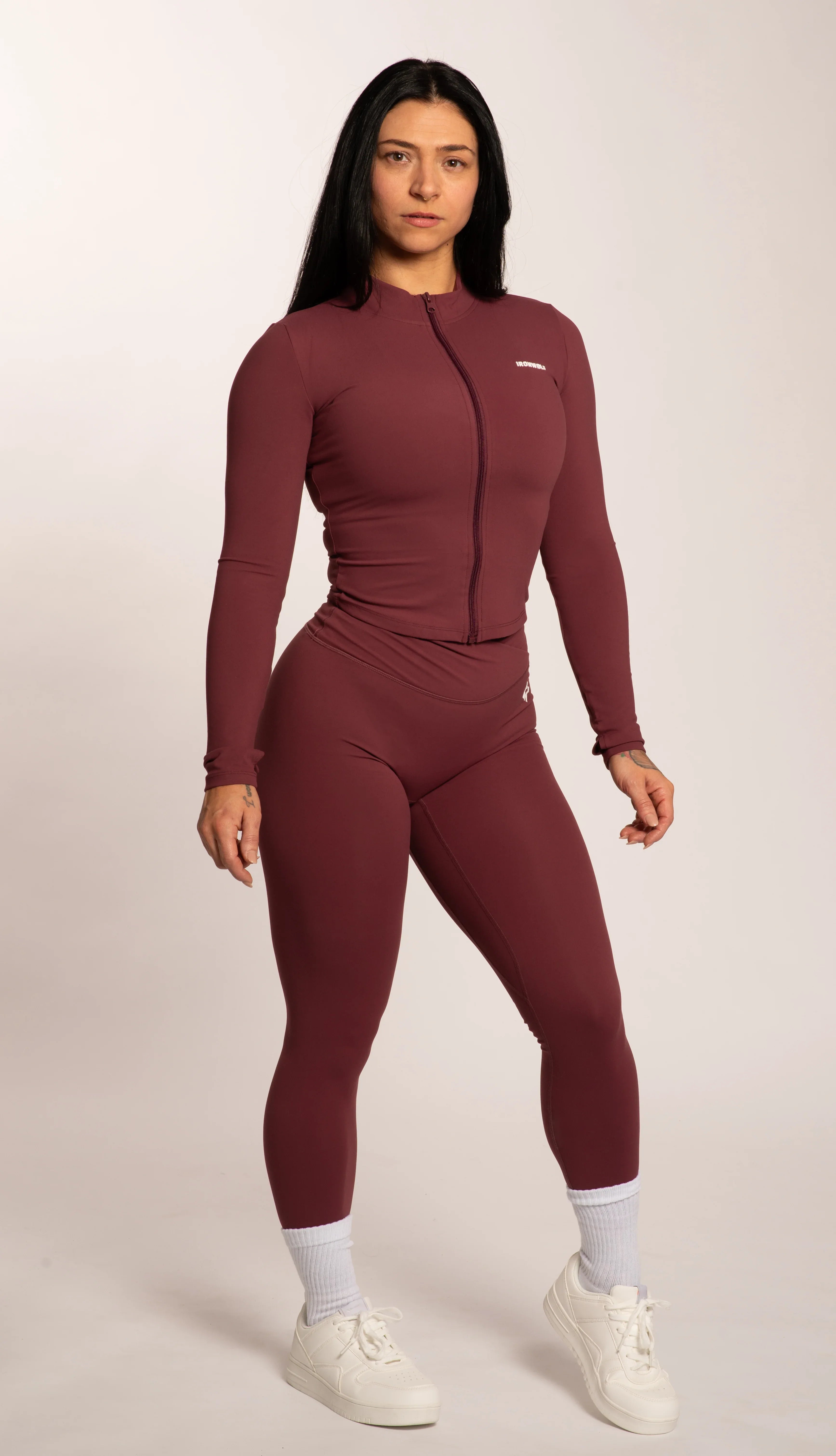 Woman in maroon gym wear set with zip-up top and leggings, styled with white sneakers for workout or casual wear