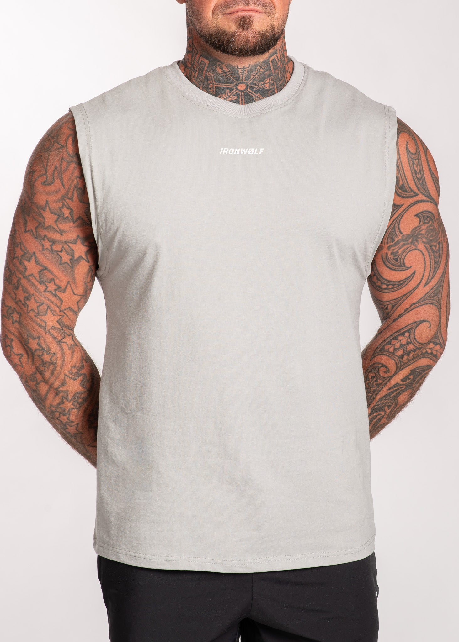 Man wearing light gray IRONWØLF sleeveless gym tank top, showcasing tattoos and athletic fit