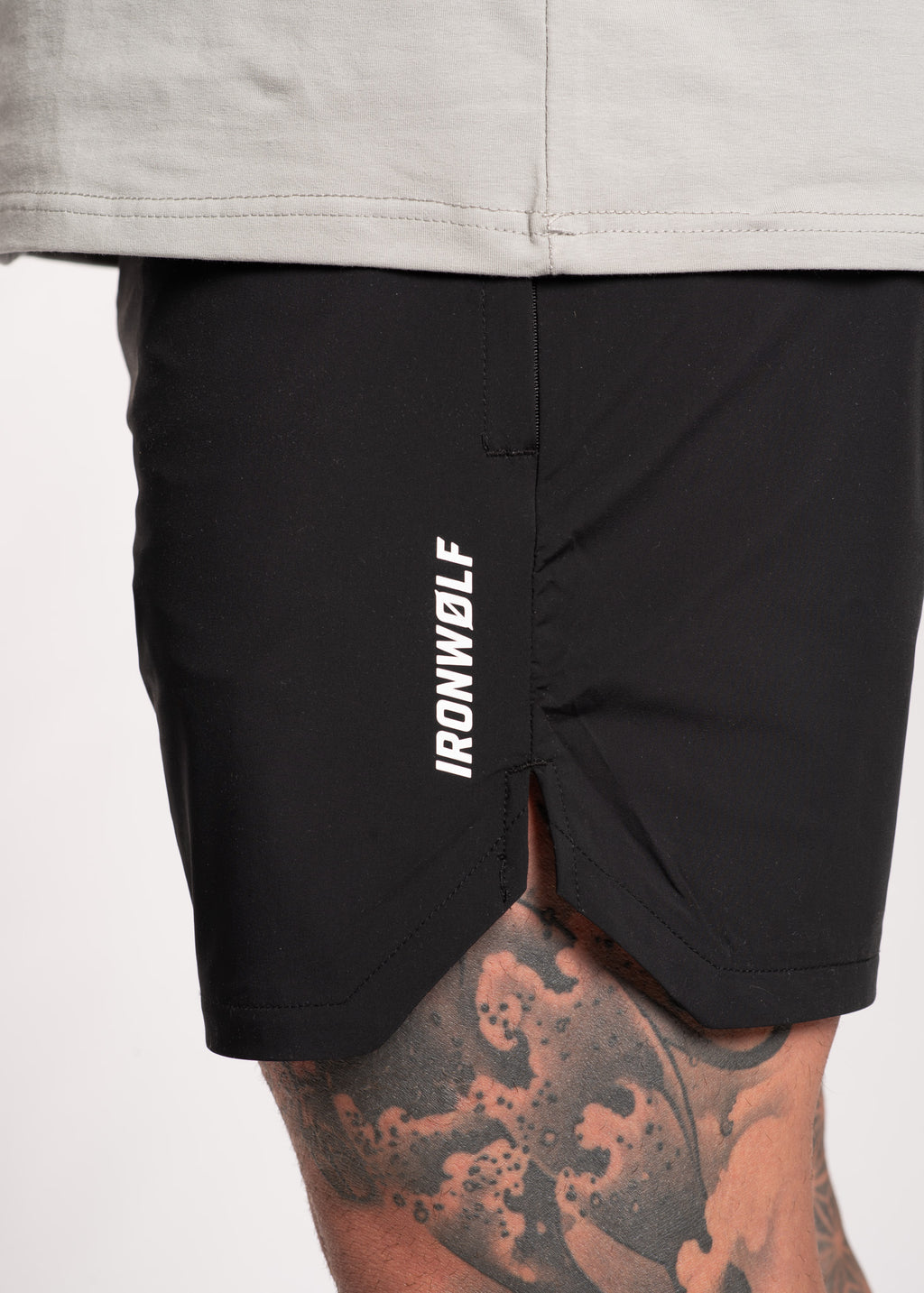 Black IRONWØLF gym shorts with side logo, worn with gray tee, showcasing athletic fit and tattooed leg