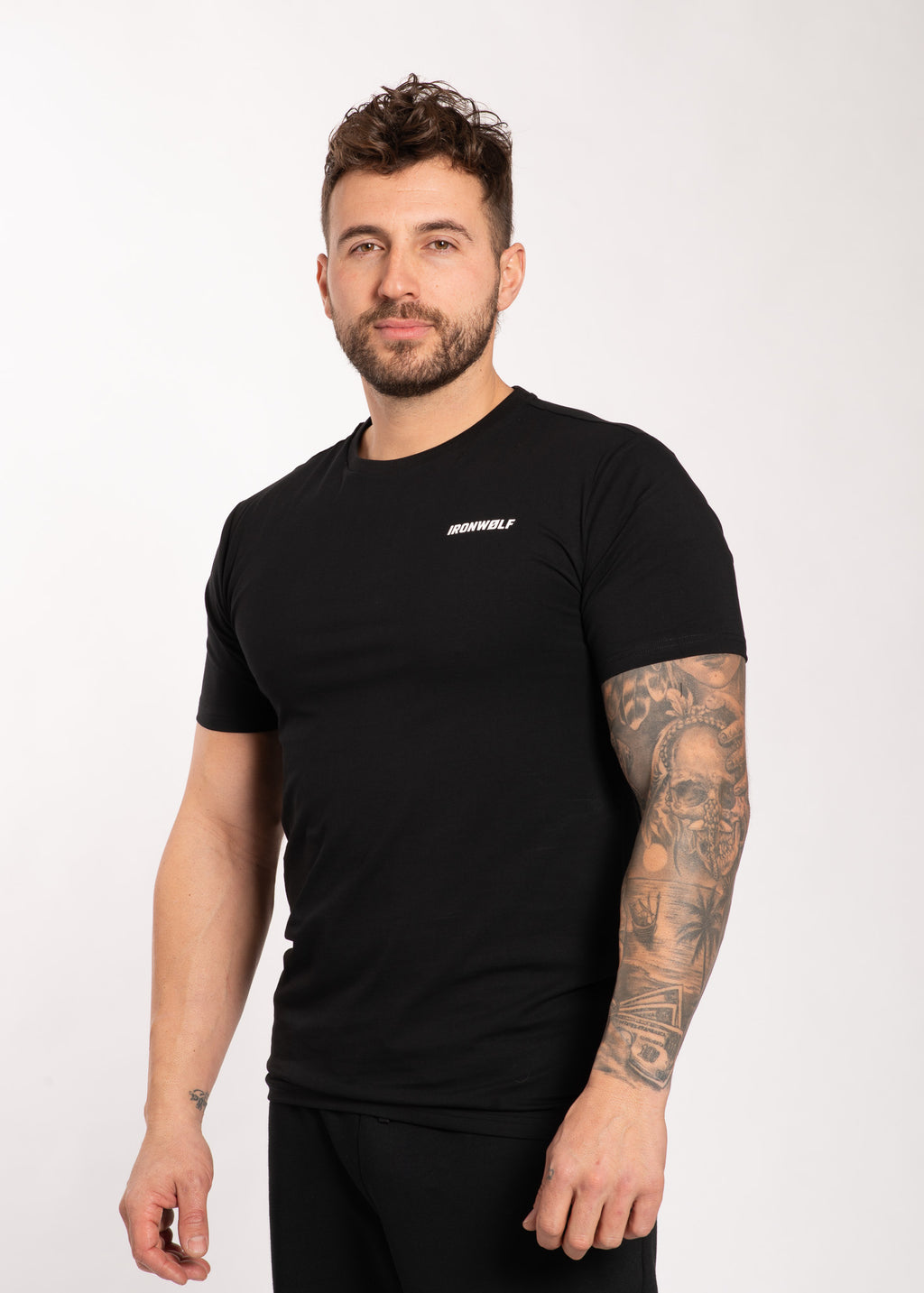 Man wearing black IRONWØLF gym t-shirt with tattooed arm, showcasing athletic activewear for training and lifestyle.