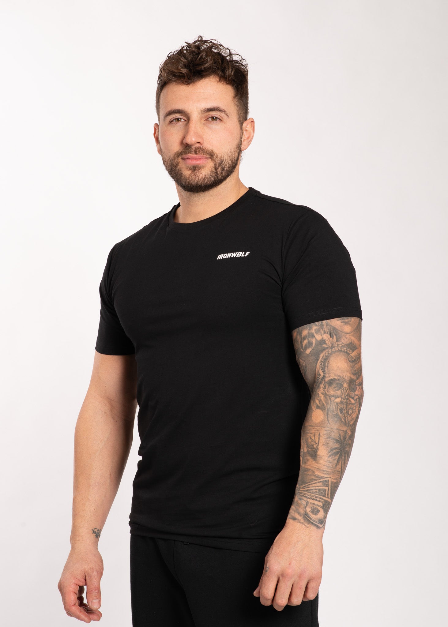 Man wearing black IRONWØLF gym t-shirt with tattooed arm, showcasing athletic activewear for training and lifestyle.
