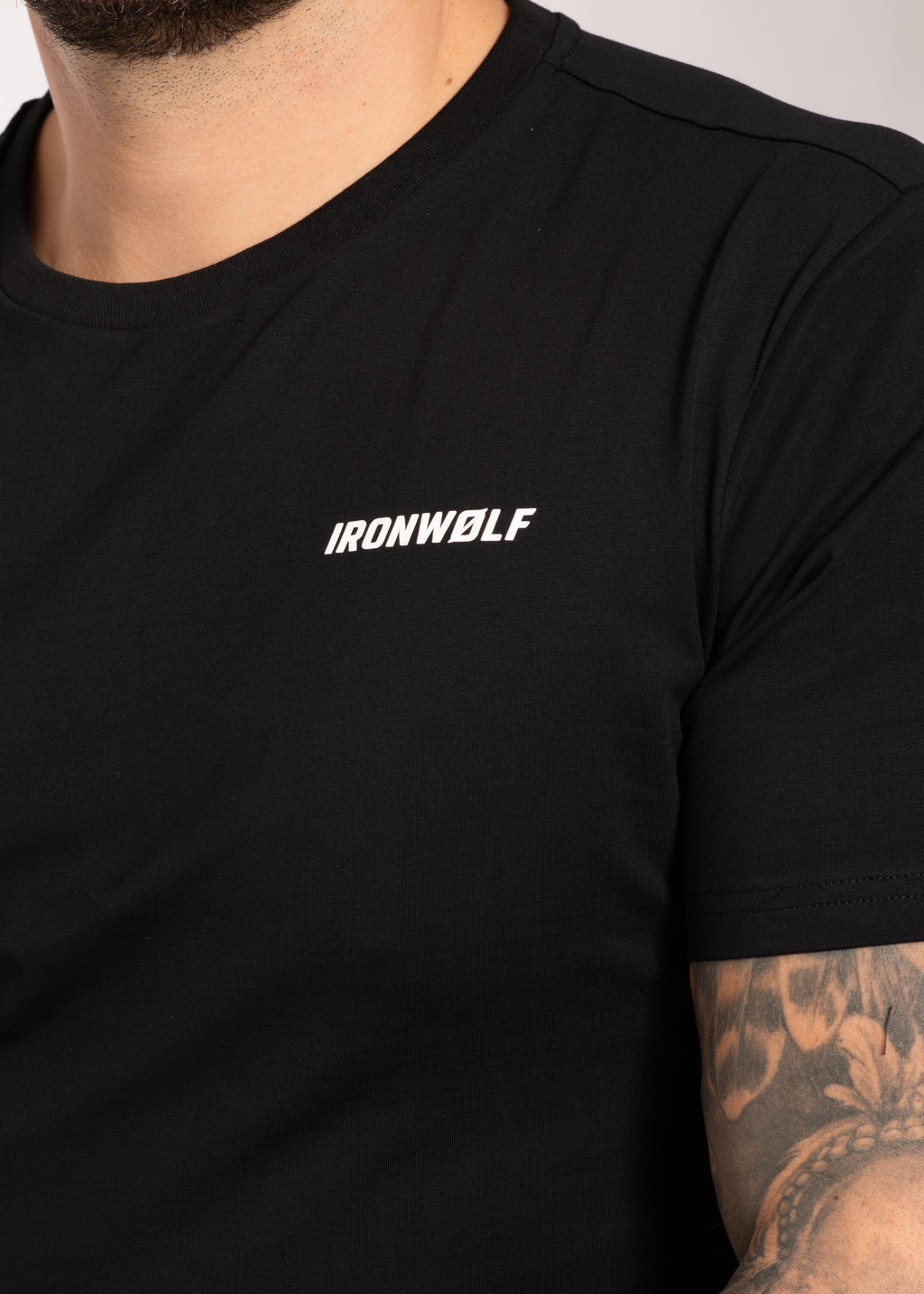 Black IRONWØLF gym t-shirt with white logo, worn by man with tattooed arm, ideal for training and active lifestyle.
