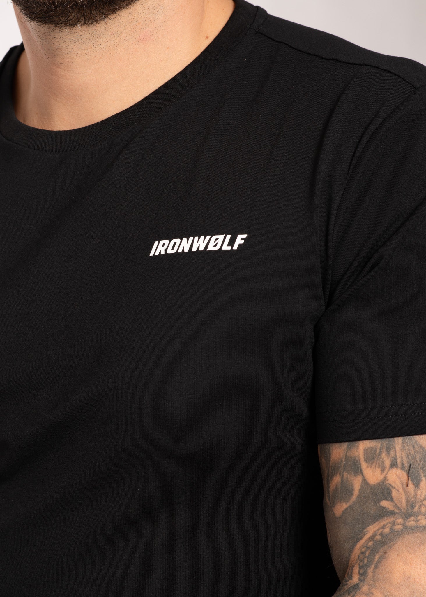 Black IRONWØLF gym t-shirt with white logo, worn by man with tattooed arm, ideal for training and active lifestyle.