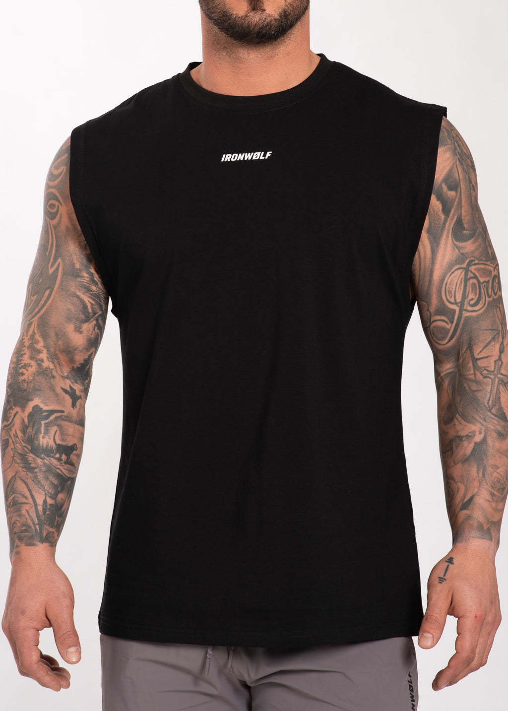Man wearing black IRONWØLF sleeveless gym shirt with chest logo, showcasing tattooed arms and athletic fit.