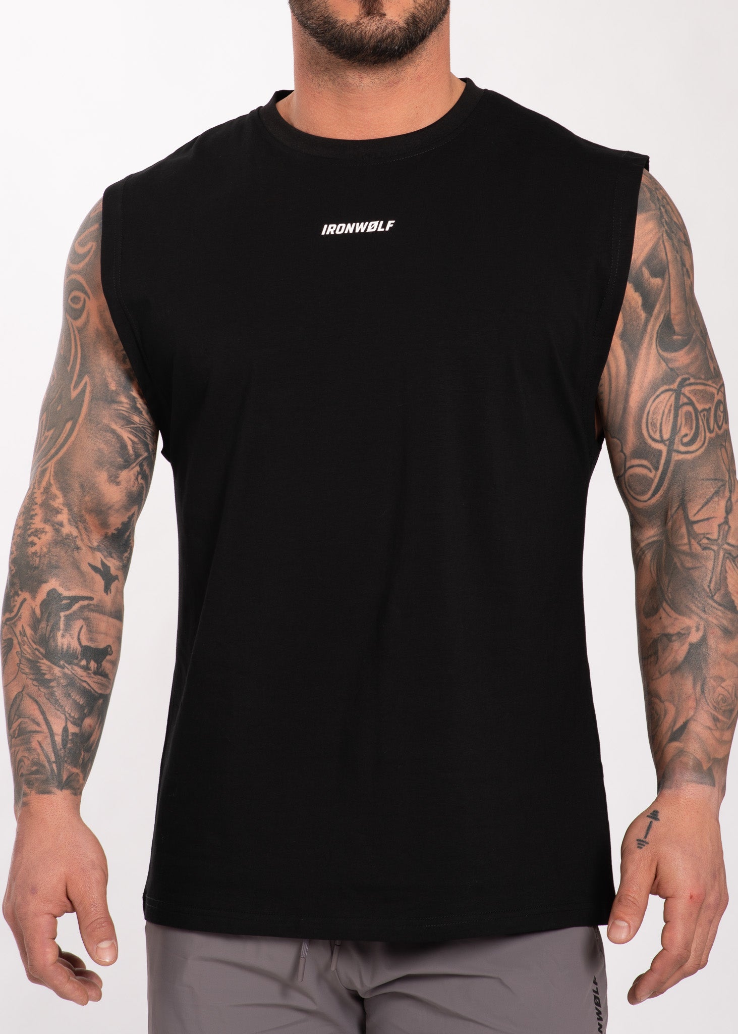 Man wearing black IRONWØLF sleeveless gym shirt with chest logo, showcasing tattooed arms and athletic fit.