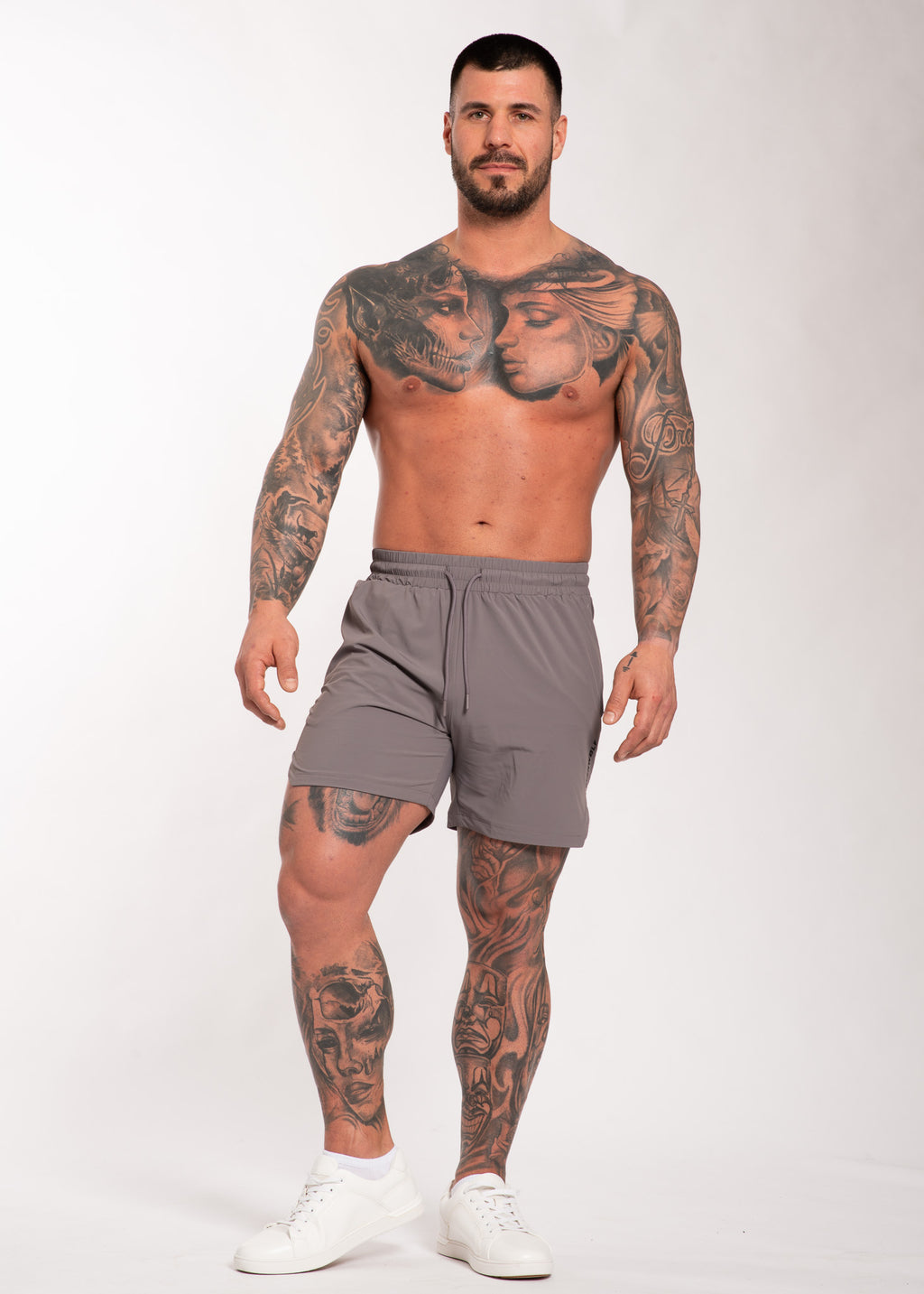 Muscular man with full body tattoos wearing gray gym shorts and white sneakers for training or lifestyle wear
