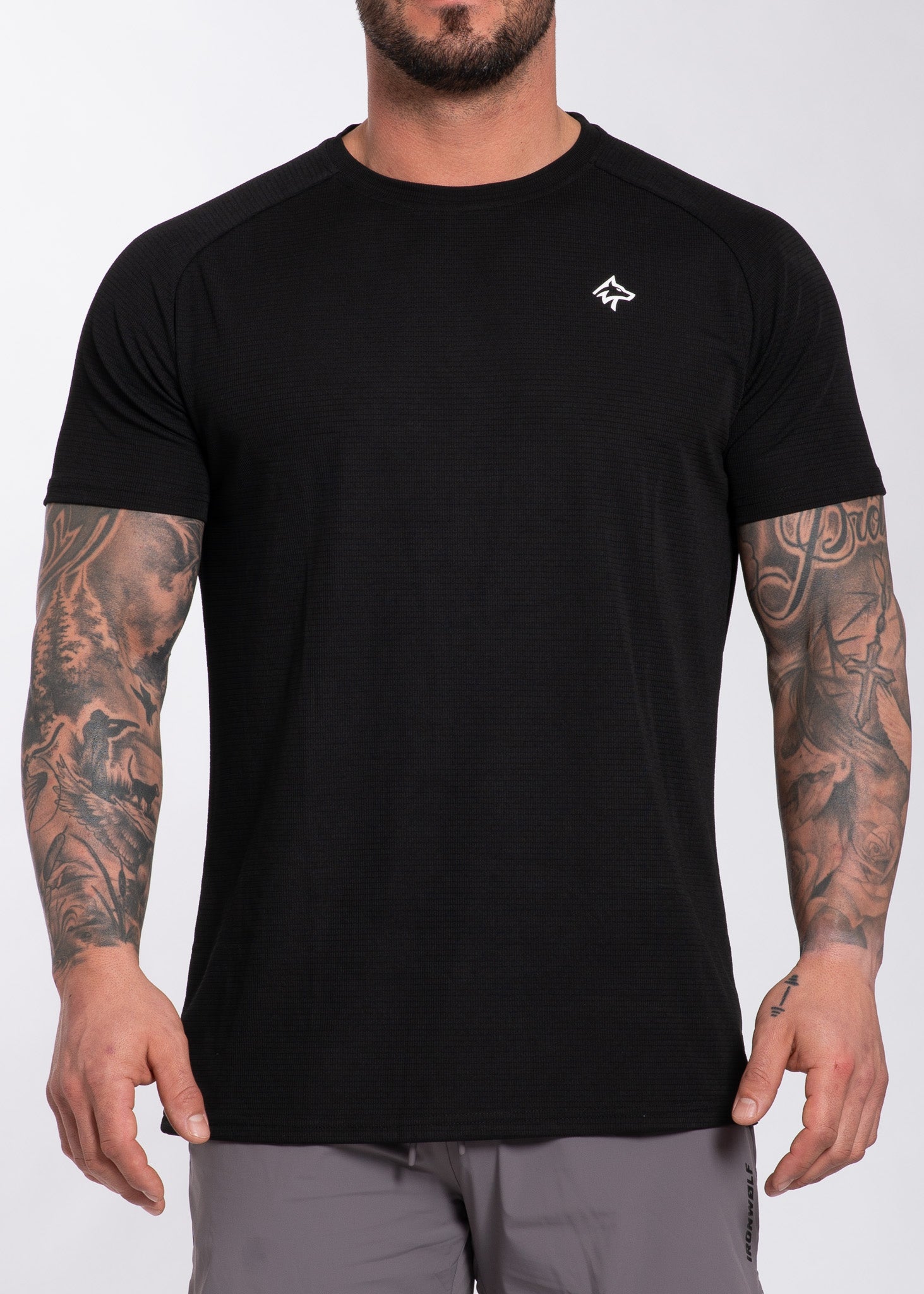 Black performance gym t-shirt with textured fabric and small white logo, worn by tattooed man for training