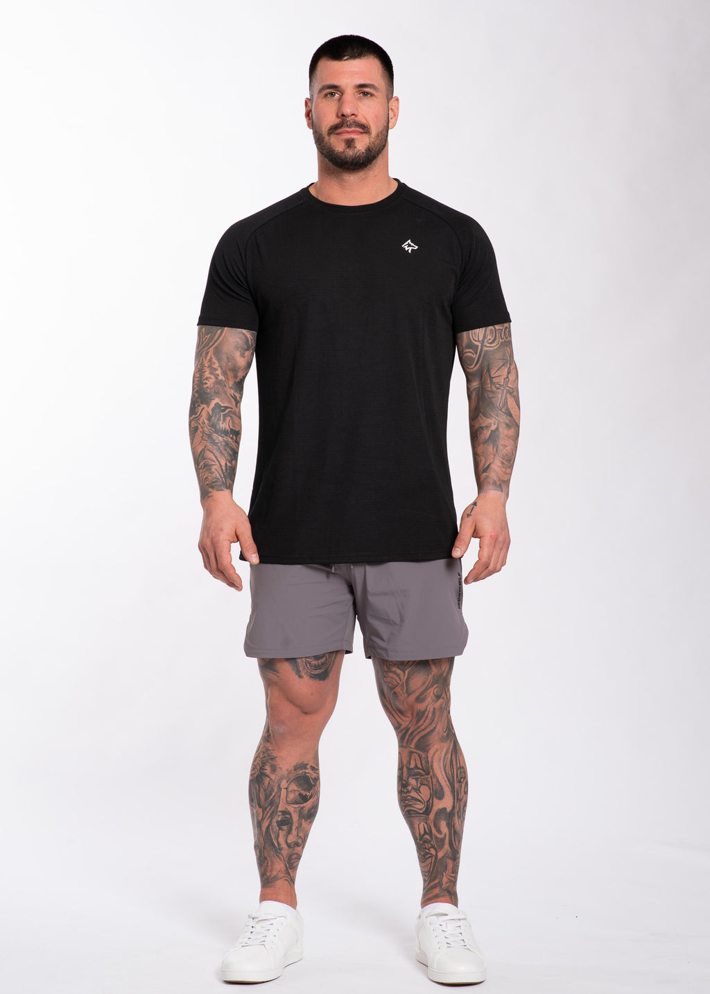 Man in black performance gym tee and gray training shorts, showcasing athletic activewear for workouts and lifestyle.