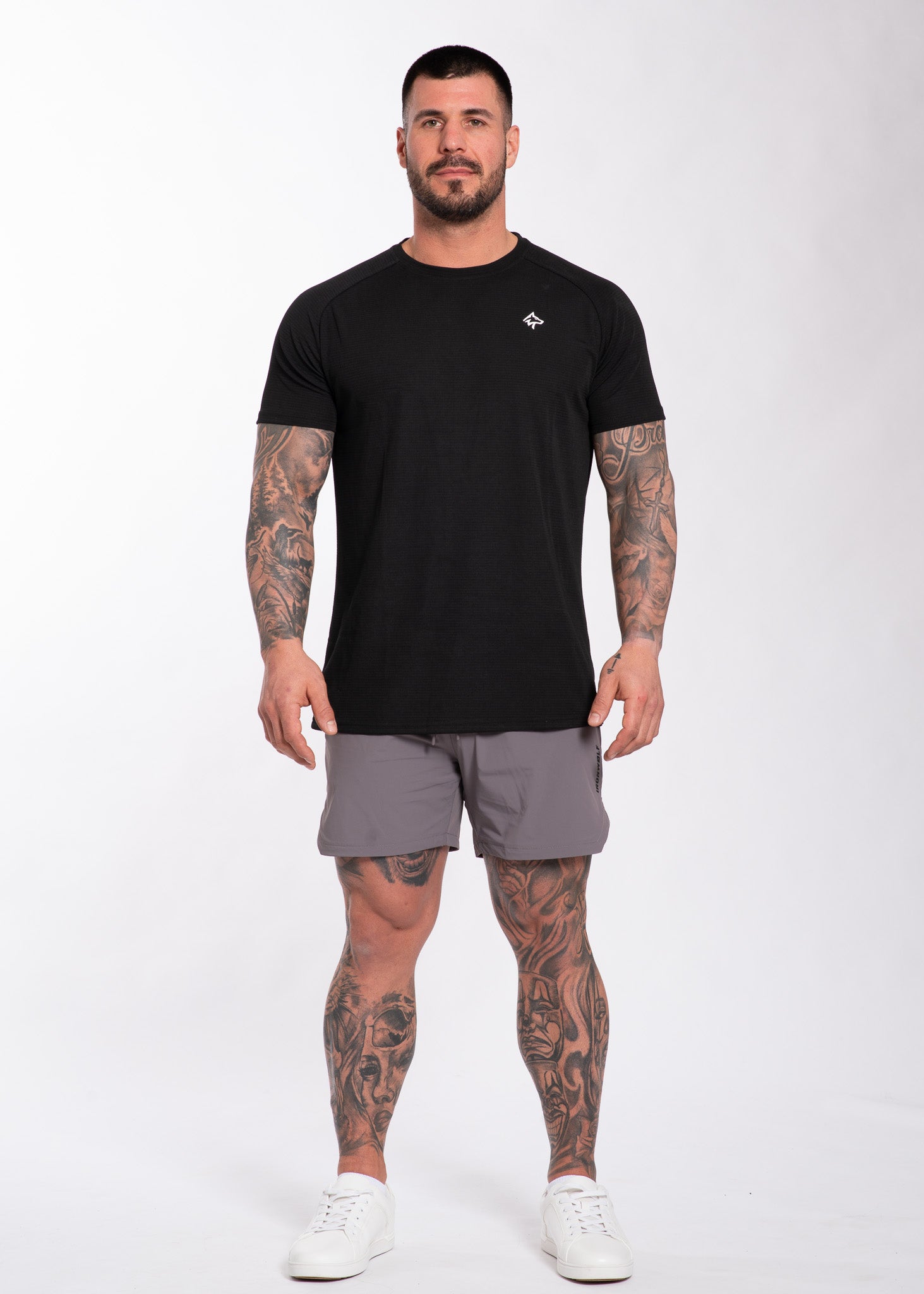 Man in black performance gym tee and gray training shorts, showcasing athletic activewear for workouts and lifestyle.