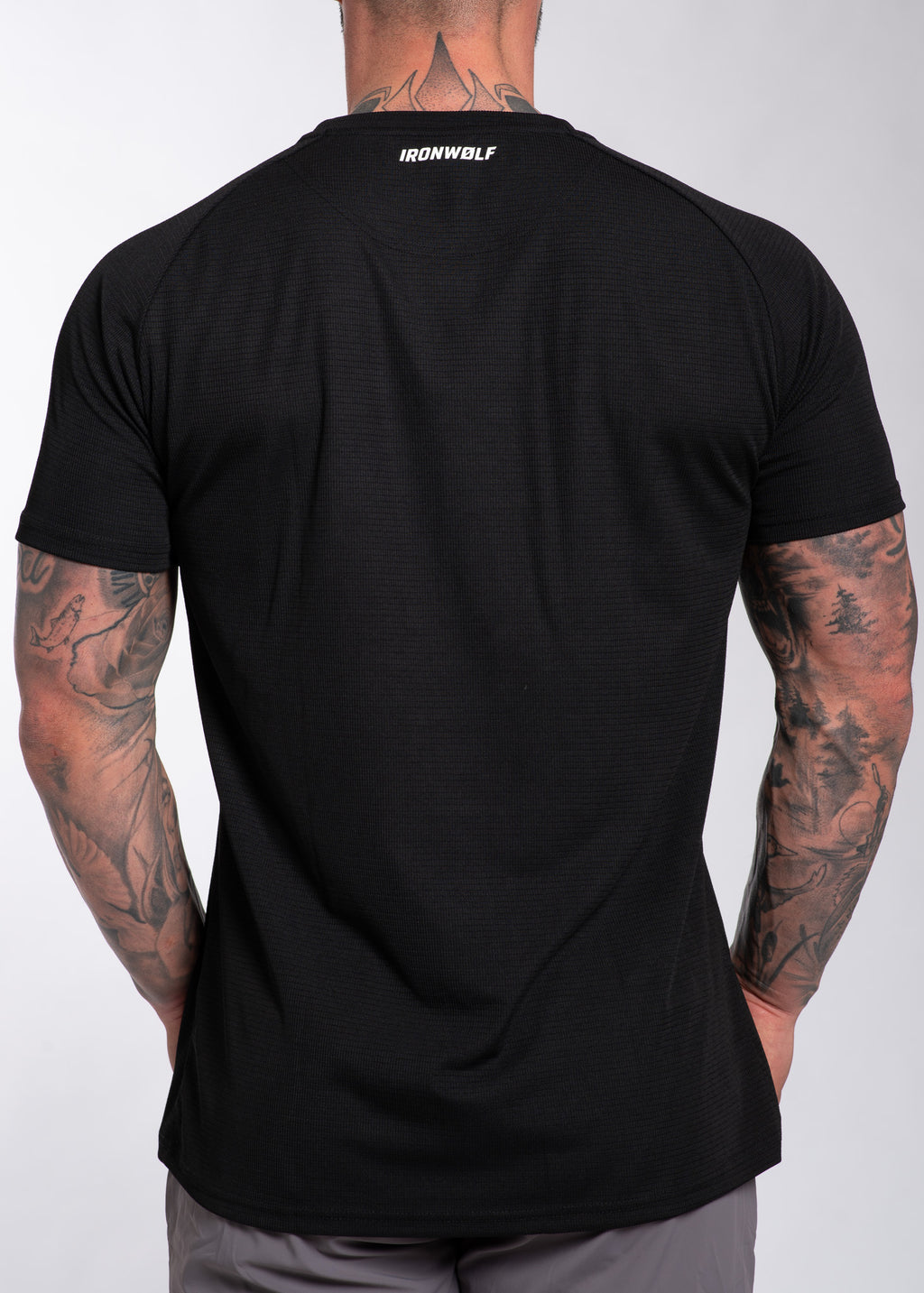 Black performance gym shirt with IRONWØLF logo, worn by tattooed man, ideal for training and active lifestyle