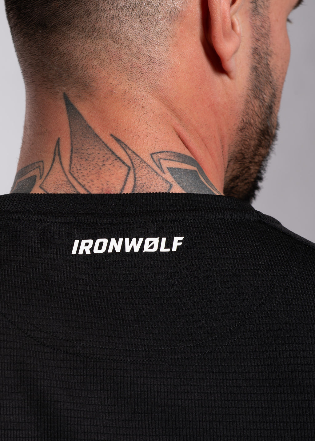 Man wearing black IRONWØLF gym shirt with neck tattoo, showcasing athletic wear for training and lifestyle