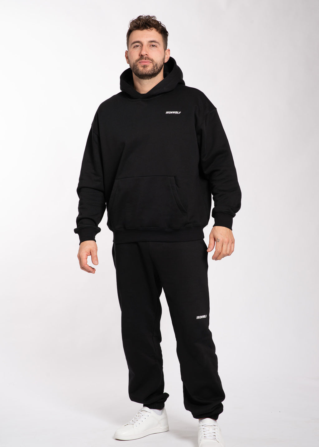 Man wearing black IRONWØLF hoodie and joggers with white sneakers, gym wear for training and lifestyle