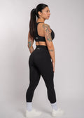 Woman in black gym wear, high-waisted leggings and sports bra, side view, tattooed arms, white sneakers
