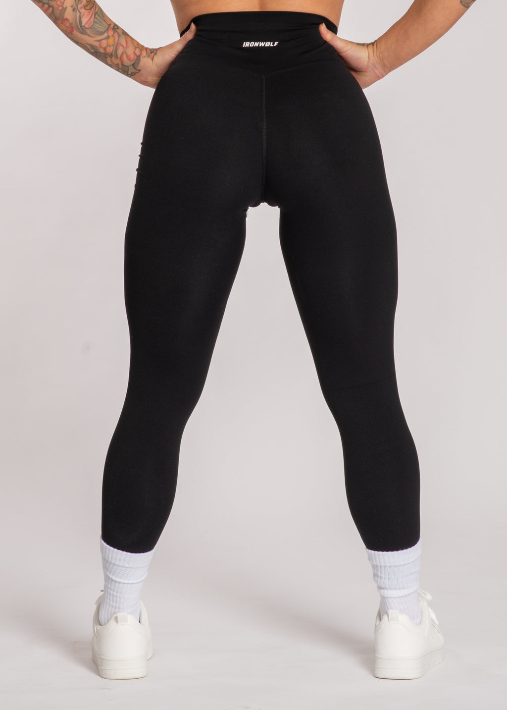 Black high-waisted gym leggings with IRONWØLF waistband, worn with white sneakers and socks for workout or lifestyle