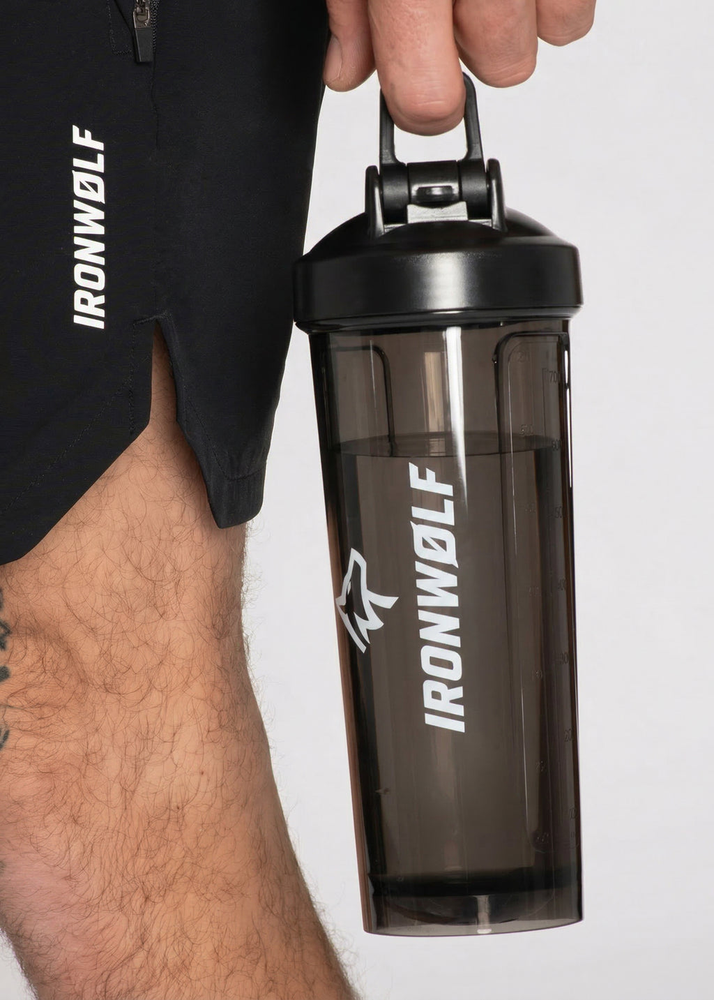 Man holding IRONWØLF shaker bottle with gym shorts, fitness gear for workouts and training