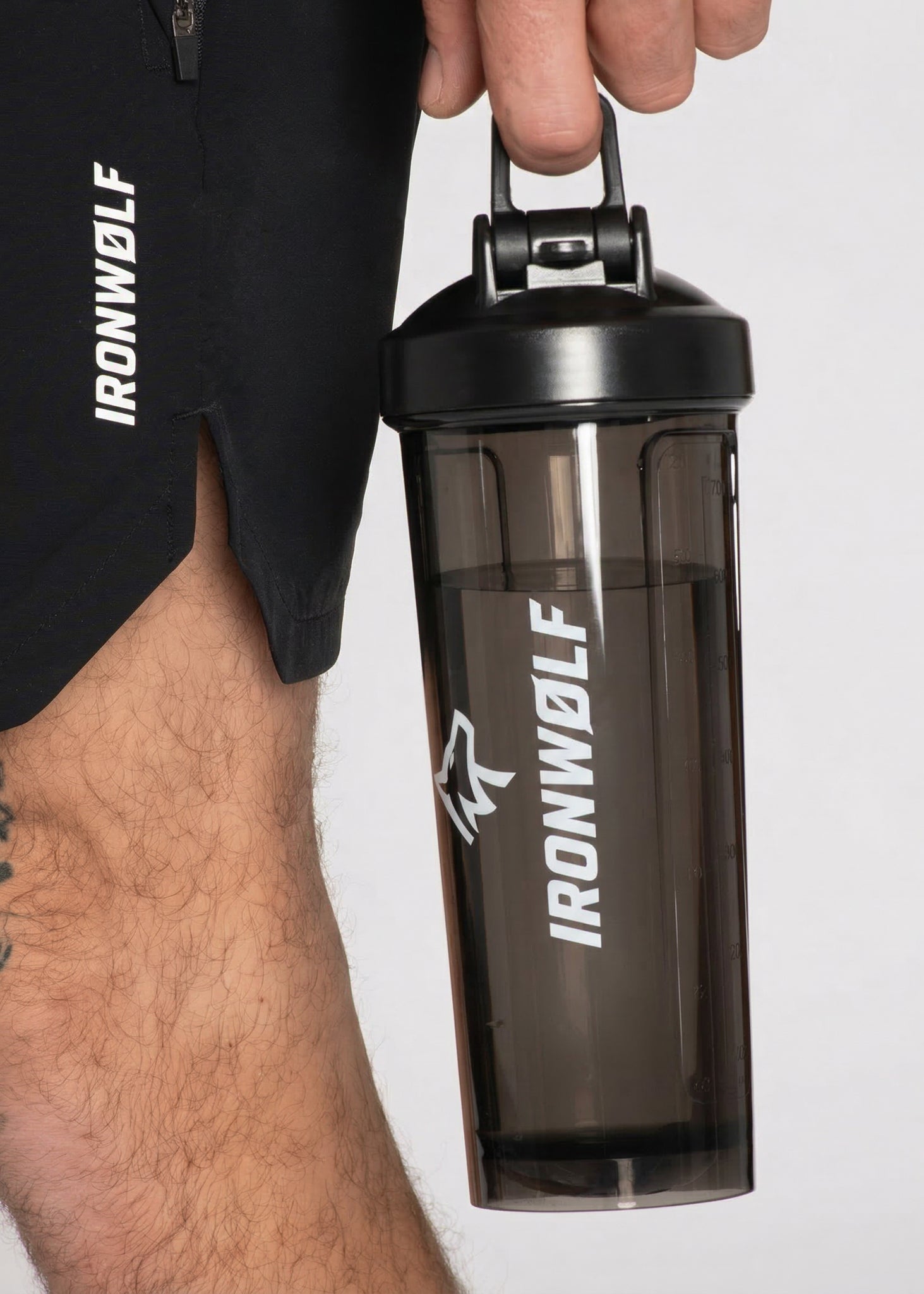 Man holding IRONWØLF shaker bottle with gym shorts, fitness gear for workouts and training