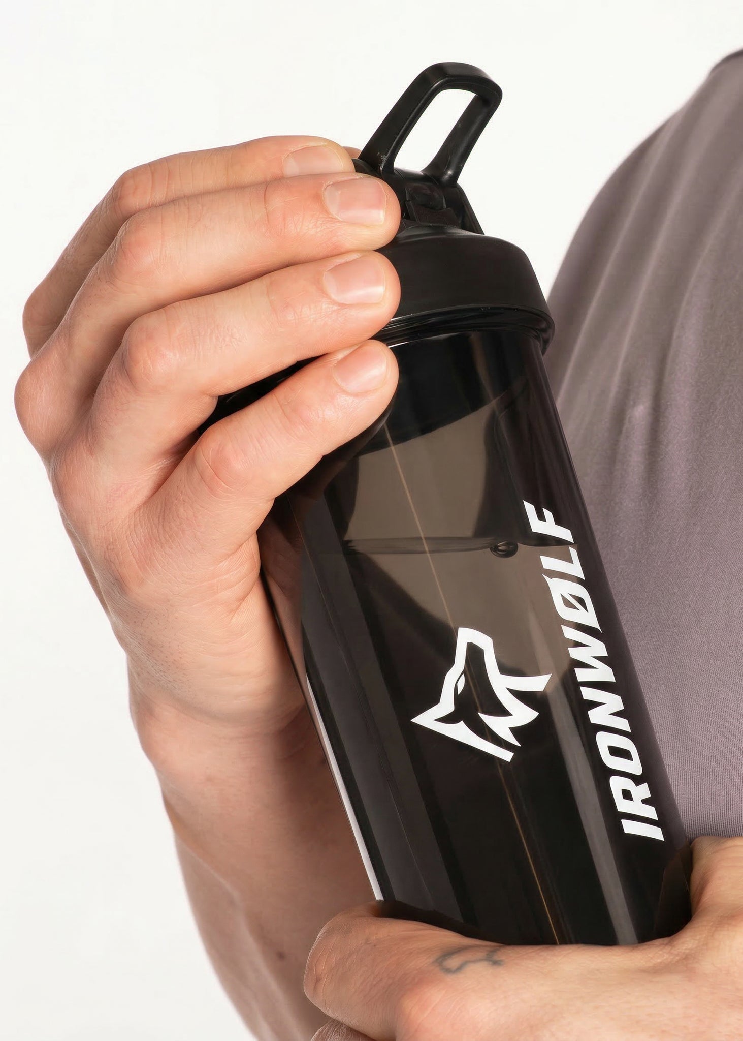 Black IRONWØLF gym shaker bottle with wolf logo, held in hand for workout hydration