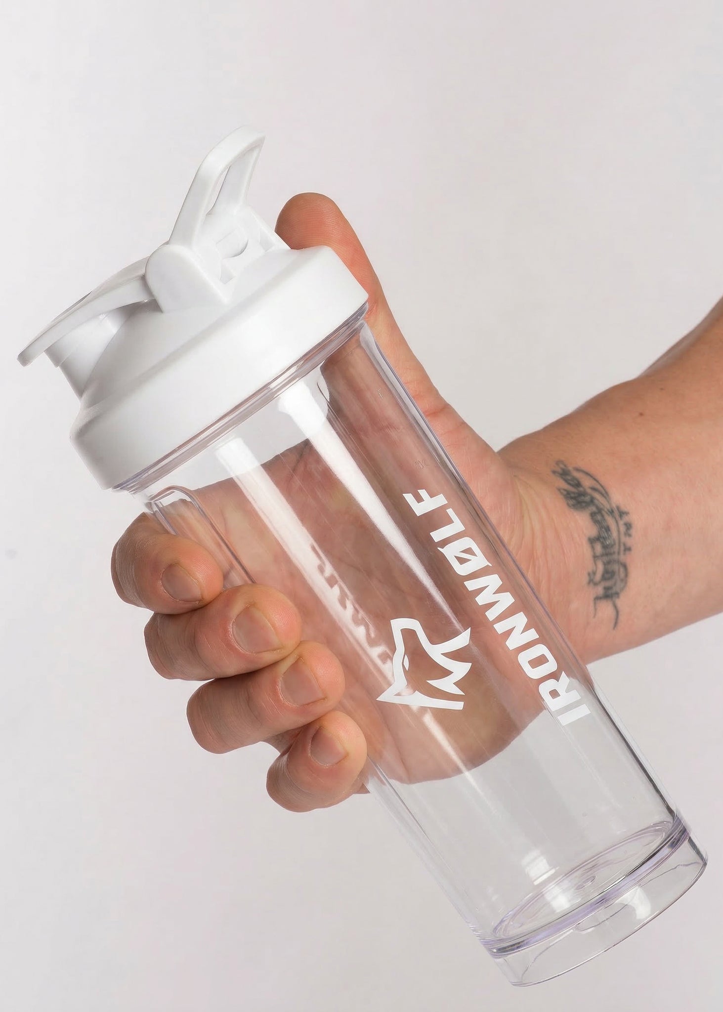 Clear shaker bottle with white lid and IRONWØLF logo, held in hand for gym or fitness use