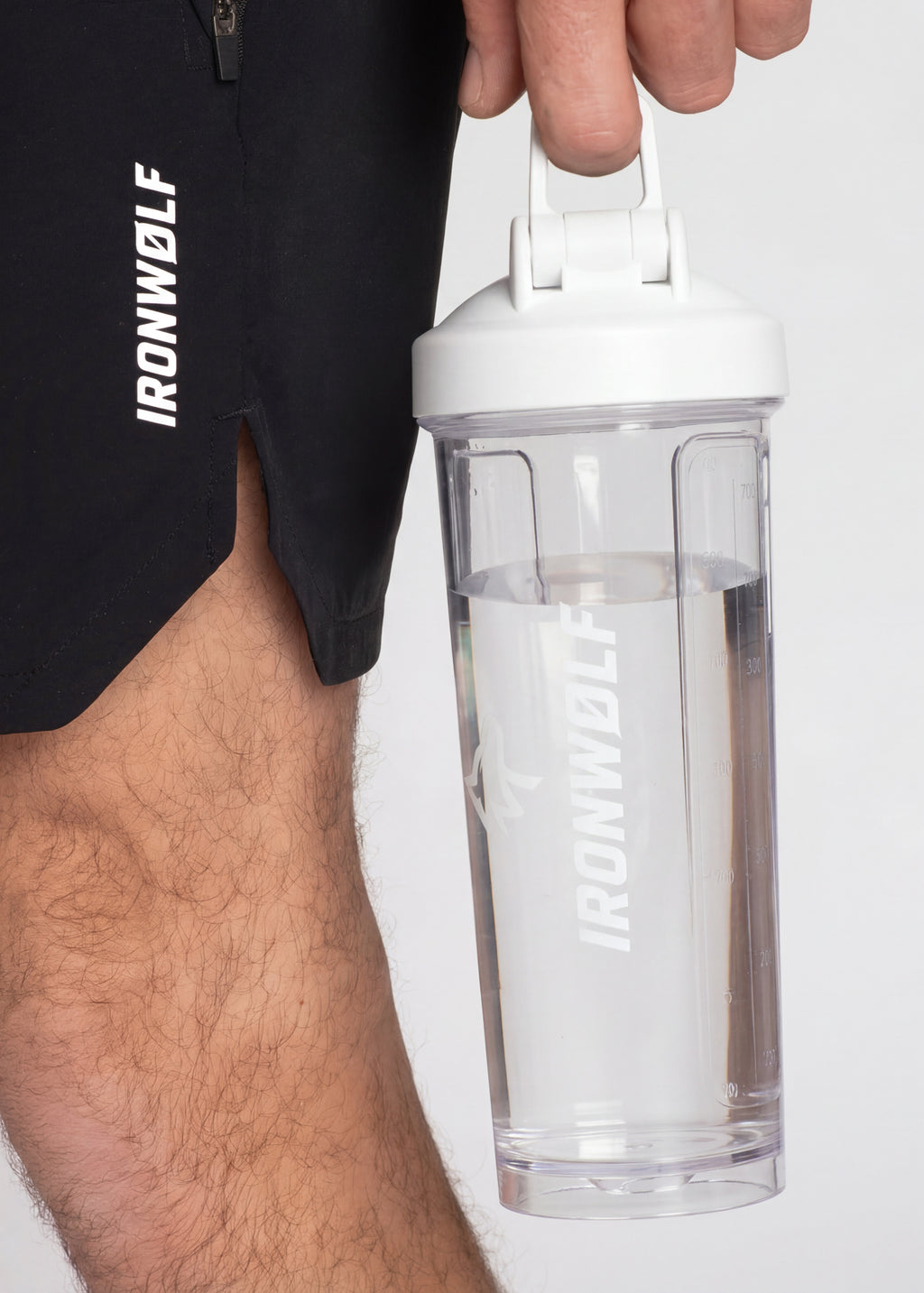 Man holding IRONWØLF shaker bottle with gym shorts, ideal for post-workout hydration and fitness routines.