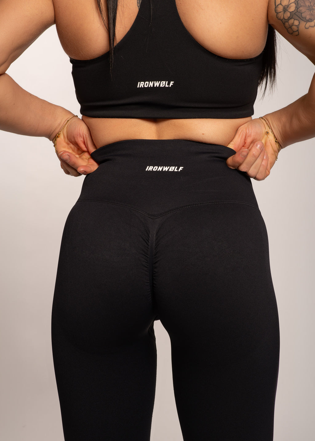 Woman in black IRONWØLF sports bra and high-waisted leggings, showcasing gym wear for training and fitness.