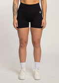 Black high-waisted gym shorts with white logo, worn with white sneakers and socks for workout or lifestyle