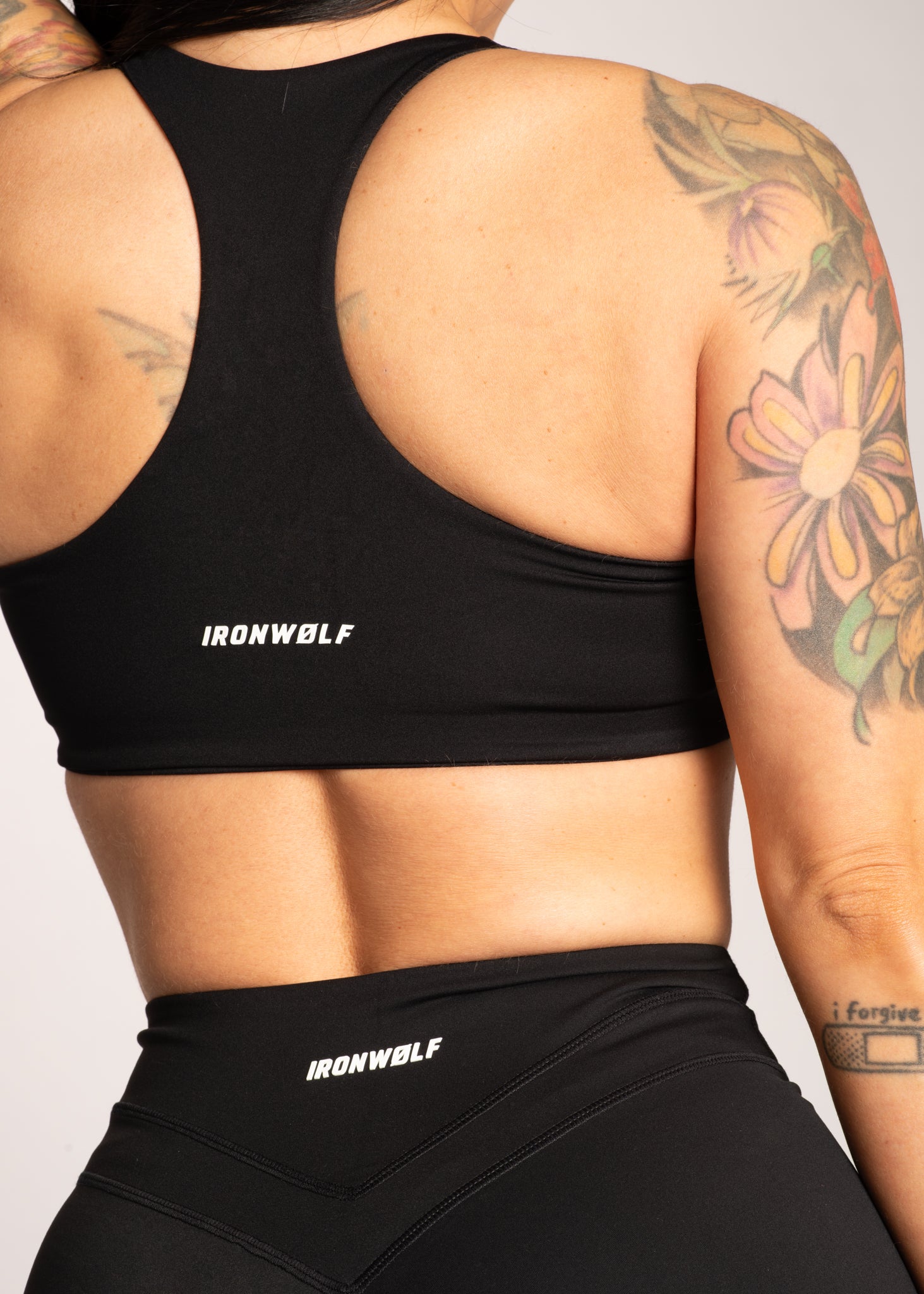 Black IRONWØLF sports bra and leggings set, showcasing back design and floral tattoos on fit woman