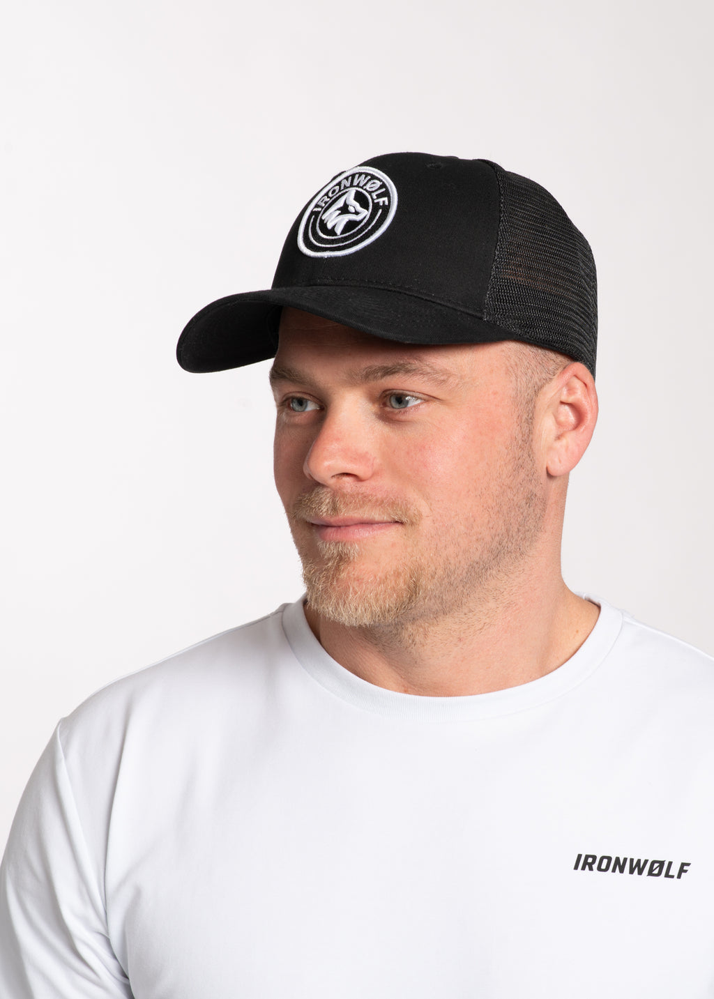 Man wearing black IRONWØLF trucker hat with white logo, paired with white activewear tee for gym or lifestyle use