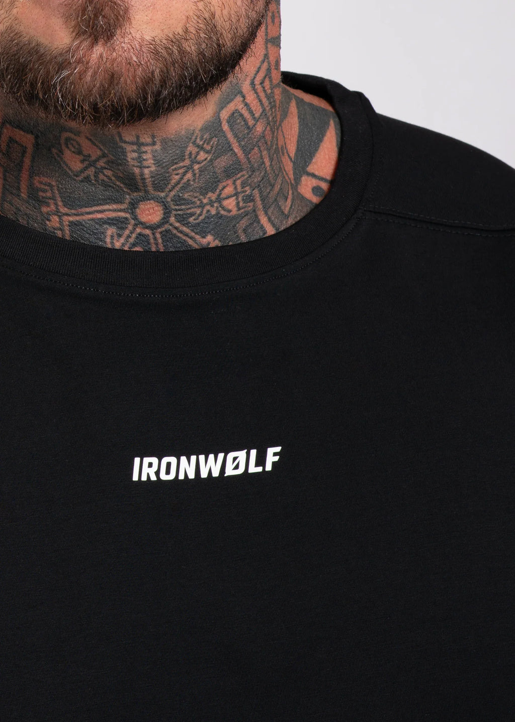 Man wearing black IRONWØLF gym tee with bold white logo, showcasing tattooed neck and beard for athletic style