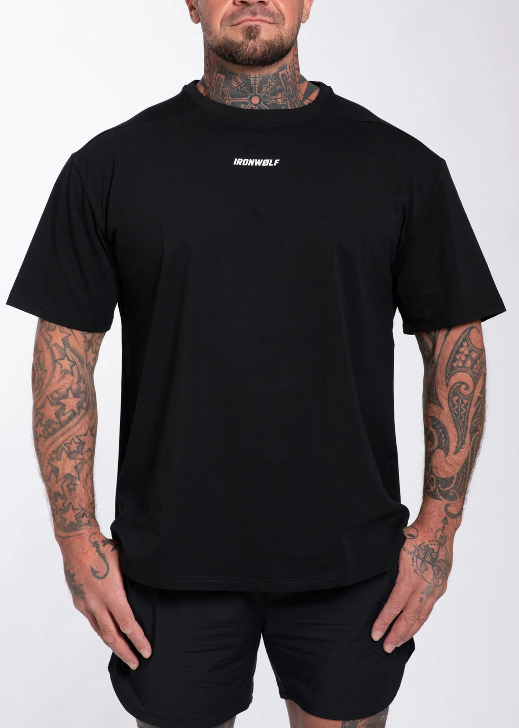 Man wearing black IRONWØLF gym t-shirt with chest logo, tattoos, and matching shorts for workout or streetwear style.