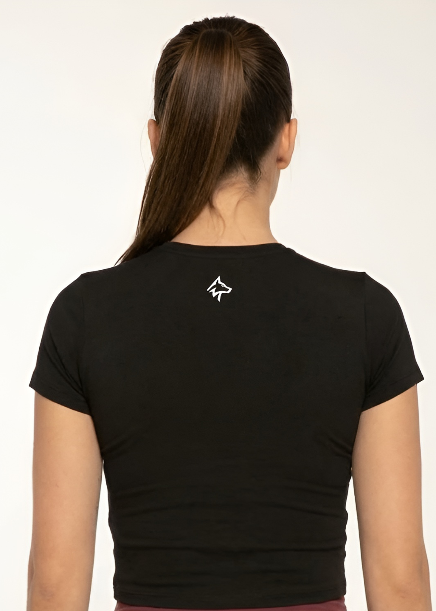 Woman wearing black cropped gym tee with white wolf logo on back, ideal for training and active lifestyle.