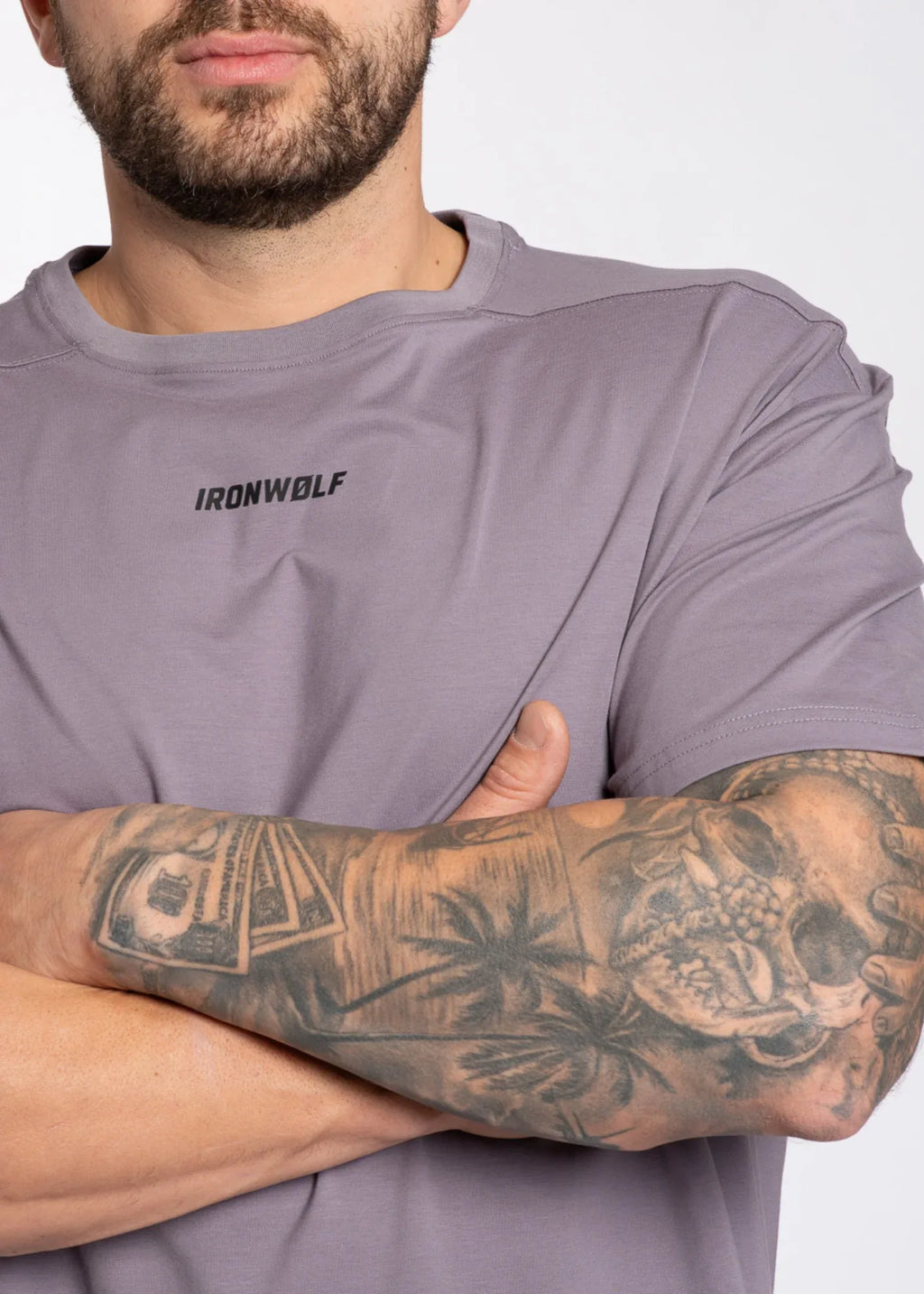 Man wearing gray IRONWØLF gym tee with tattooed arms crossed, showcasing athletic activewear style