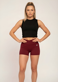 Woman in black crop top and burgundy gym shorts, hands on hips, studio fitness wear