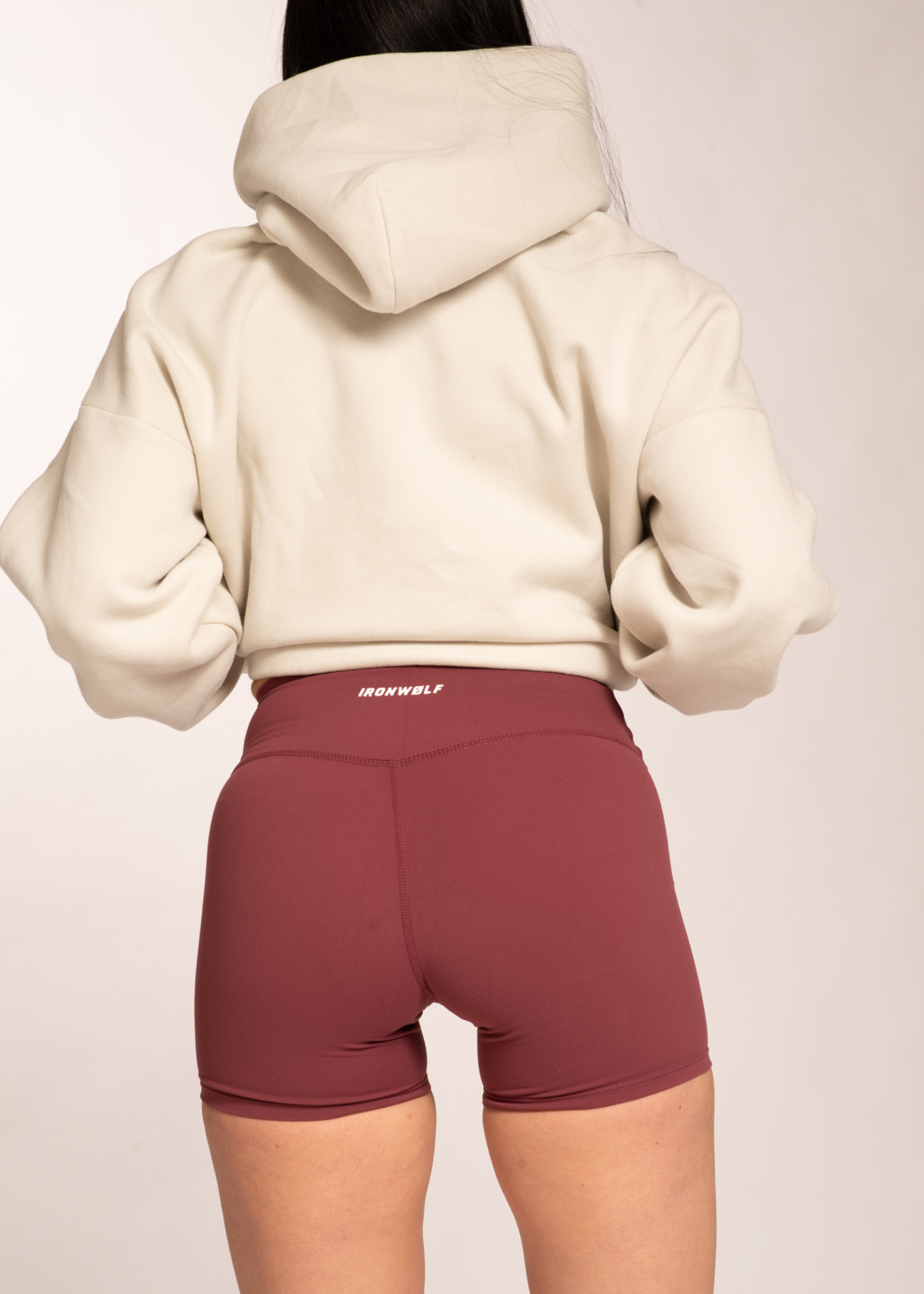 Woman in cream hoodie and burgundy high-waisted gym shorts with IRONWØLF waistband