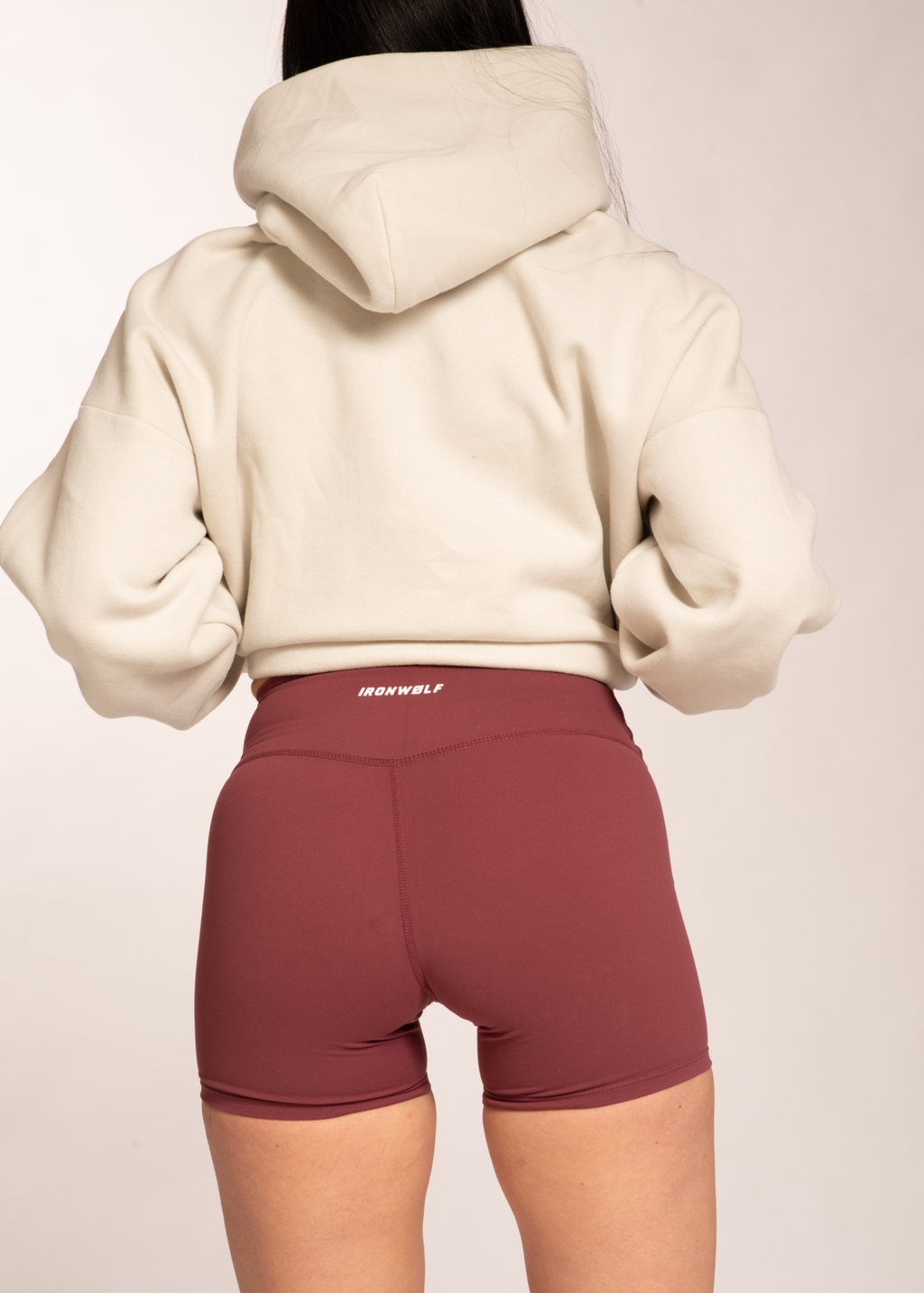 Woman wearing cream hoodie and burgundy IRONWØLF gym shorts, back view