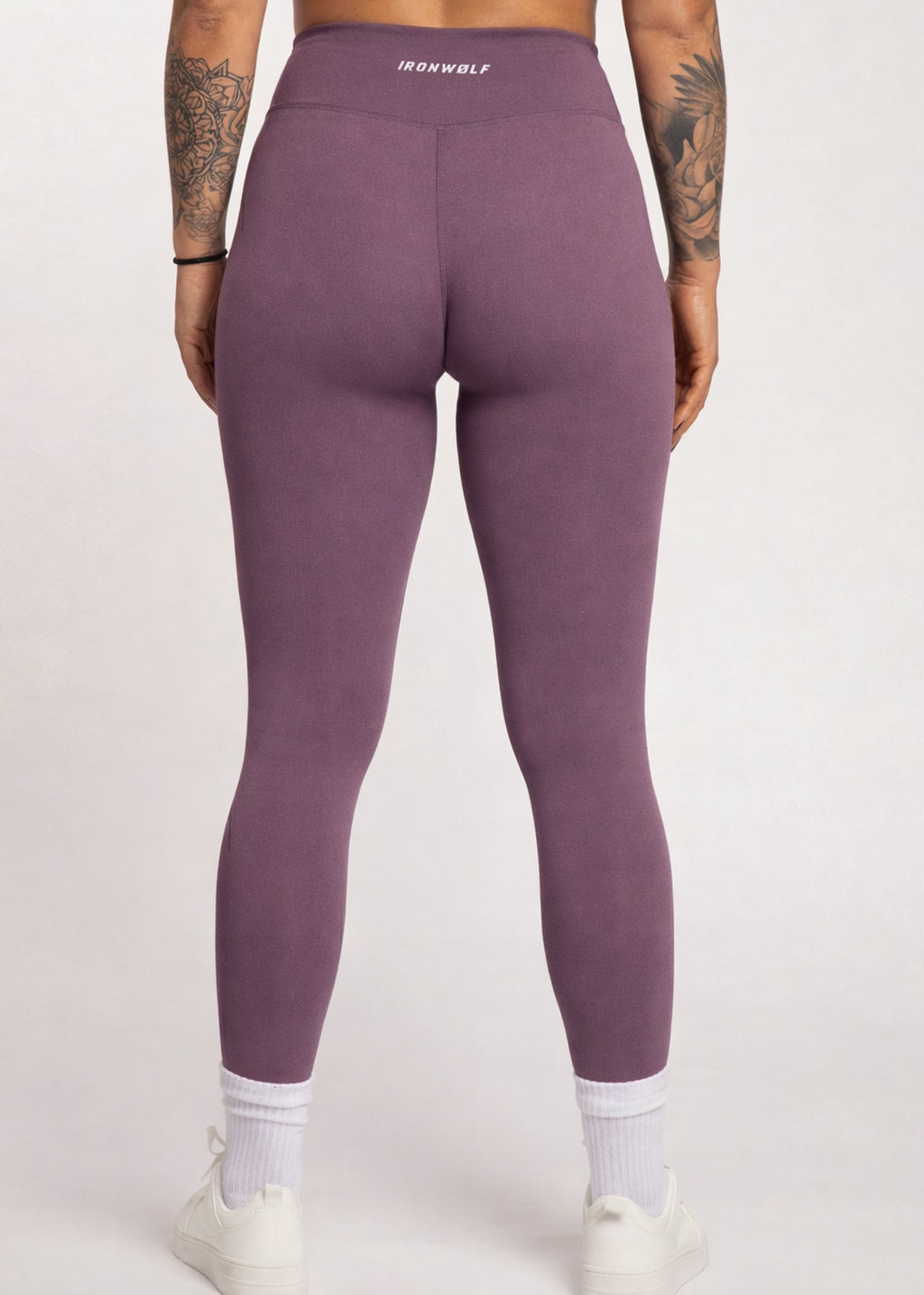 Purple high-waisted gym leggings with IRONWØLF waistband, worn with white socks and sneakers for workout or lifestyle