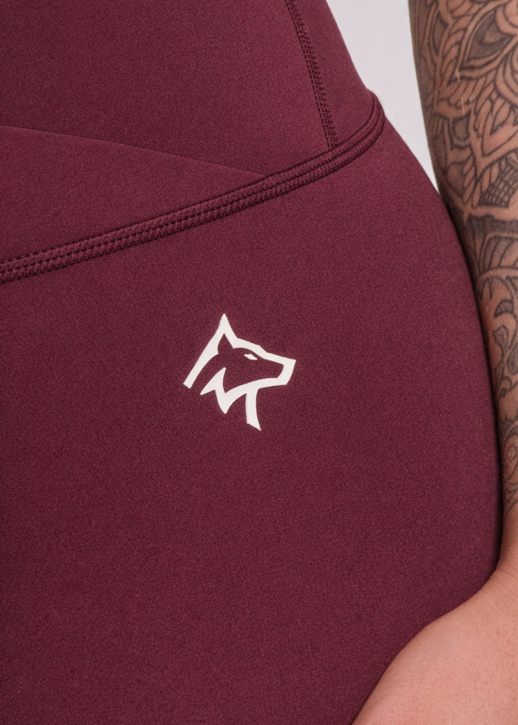 Maroon gym leggings with white wolf logo, worn by tattooed athlete for training and fitness