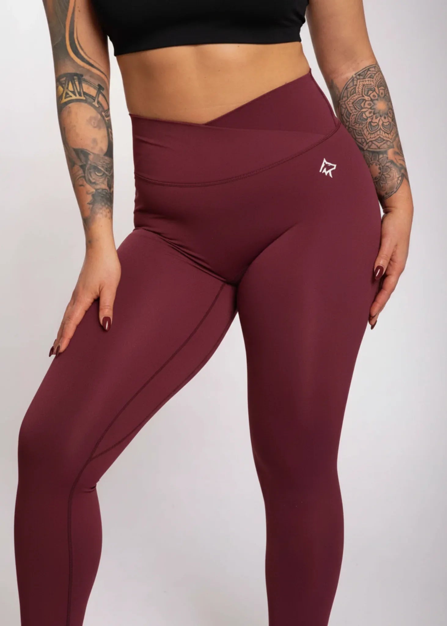 Woman in burgundy high-waisted gym leggings with tattooed arms, ideal for training and active lifestyle