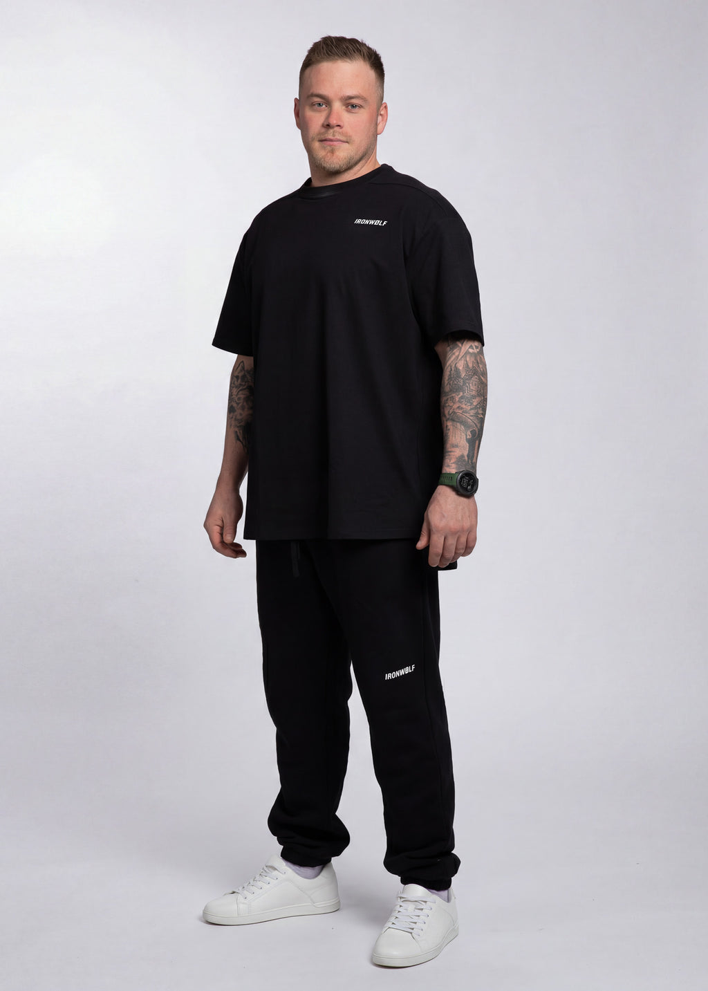 Man wearing black IRONWØLF gym tee and sweatpants with white sneakers, showcasing athletic activewear for training and lifestyle.
