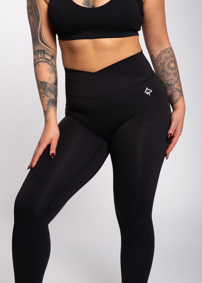 Black high-waisted gym leggings with crisscross waistband, worn with matching sports bra for workout or training